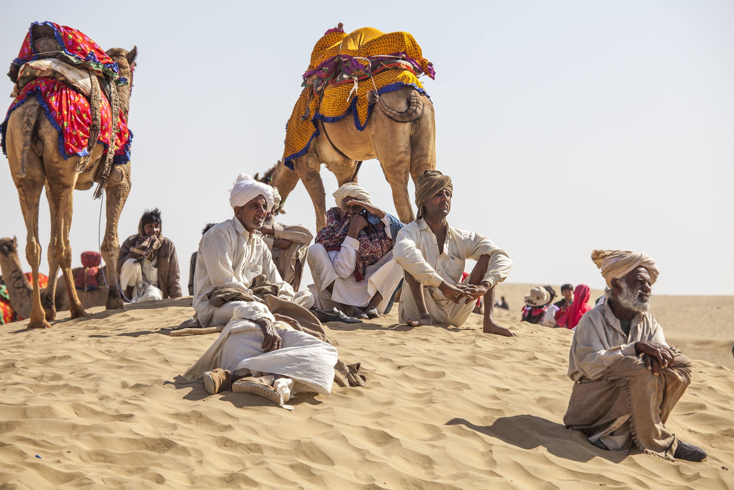 Indian men wearing turbans sitting with camels in the desert near Jaisalmer India