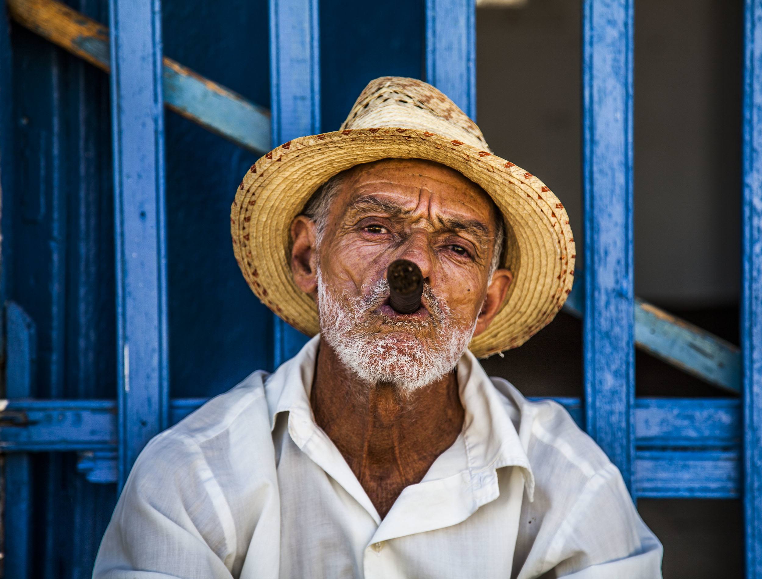 Cuban man smoking cigar in front of blue door in Trinidad Cuba