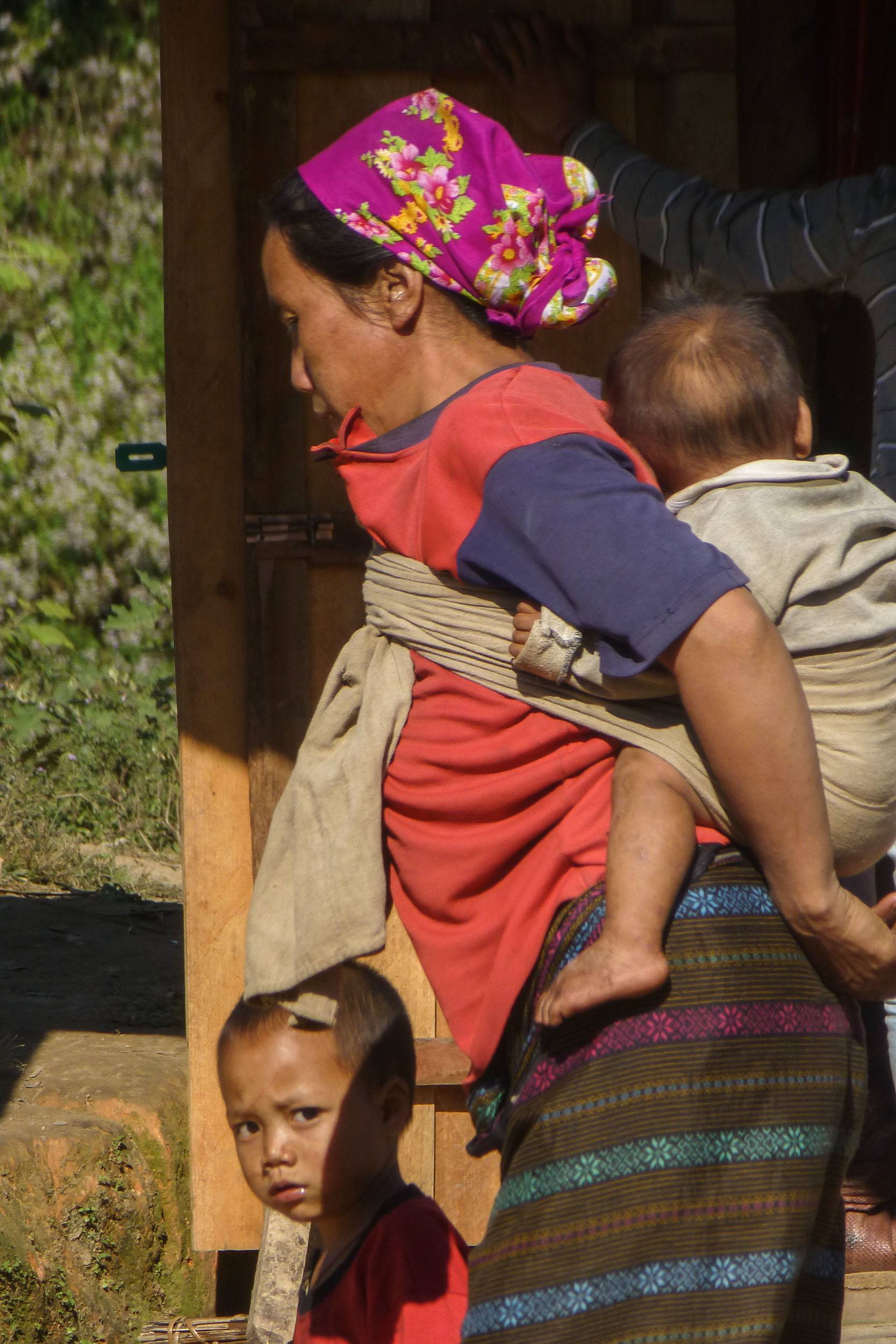 Akha woman carrying baby on her back in remote village of Laos