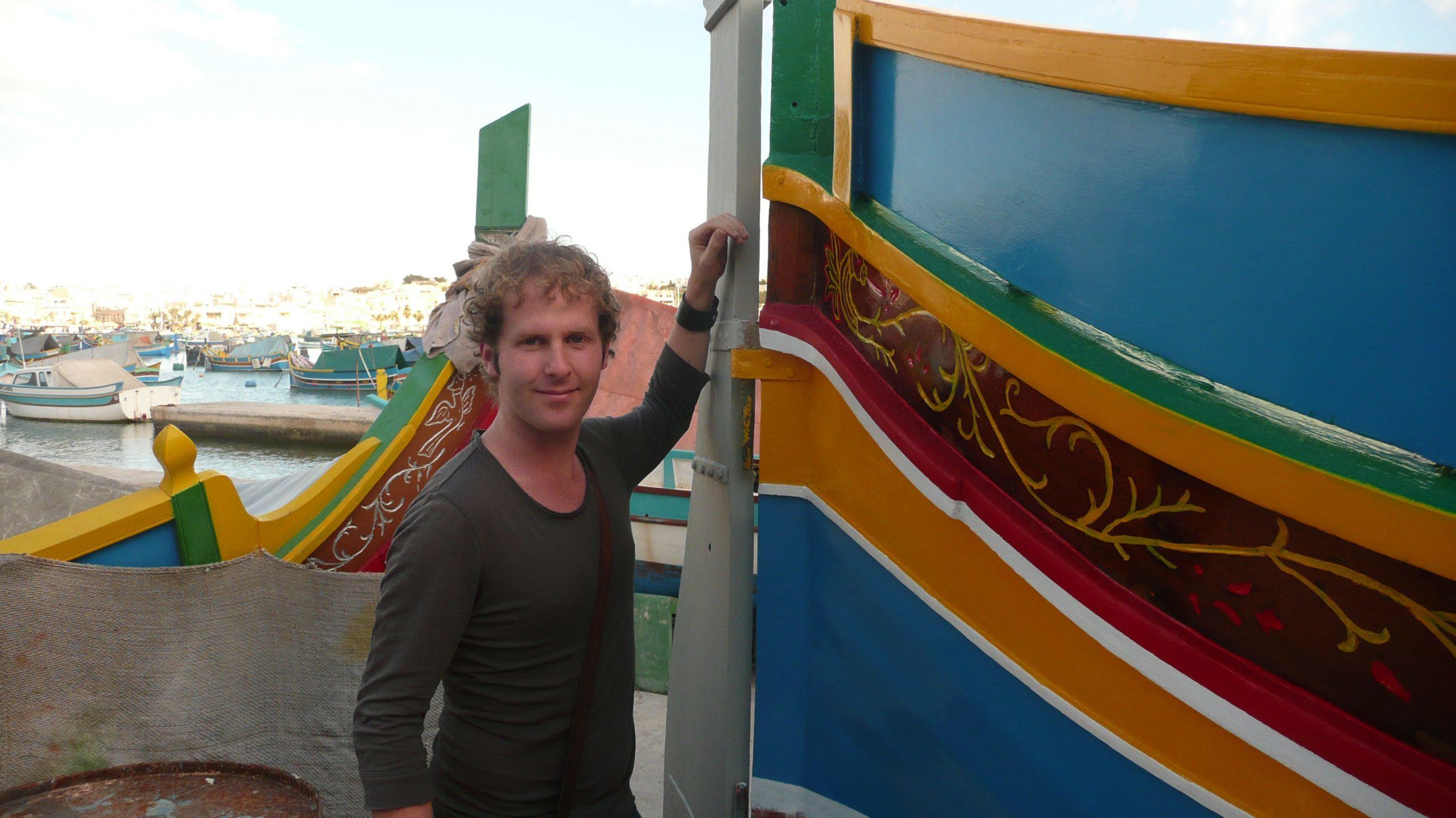 Ben beside colourful boat in Marsaxlokk Malta