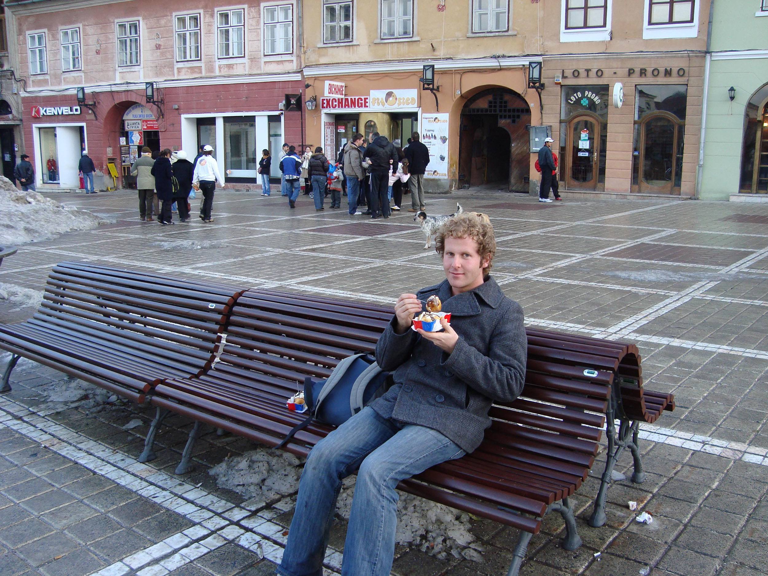 Ben eating dessert sitting on a bench in Piata Sfatului Brasov Romania