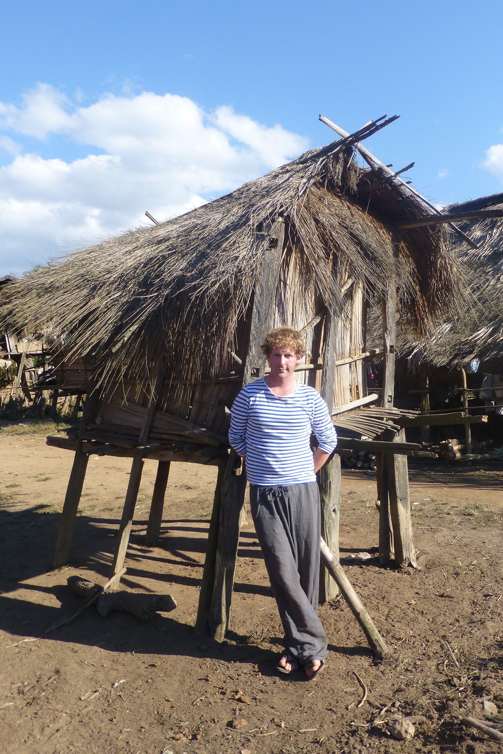 Ben leaning against straw hut in Akha village in Laos