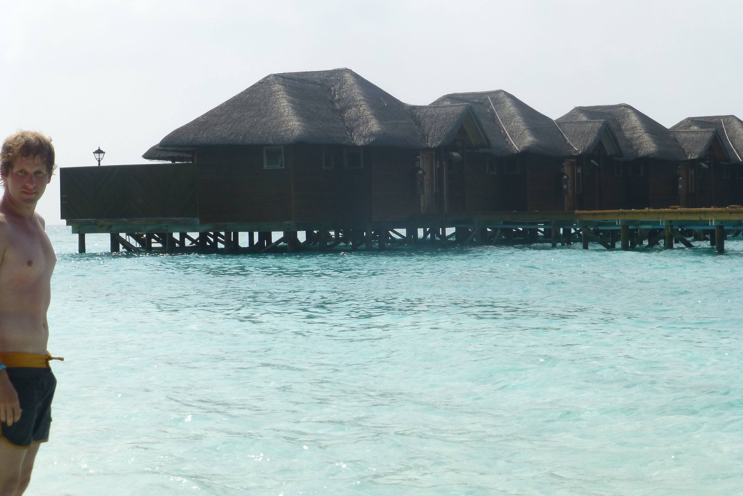 Ben standing in front of overwater bungalows on Fihalhohi the Maldives