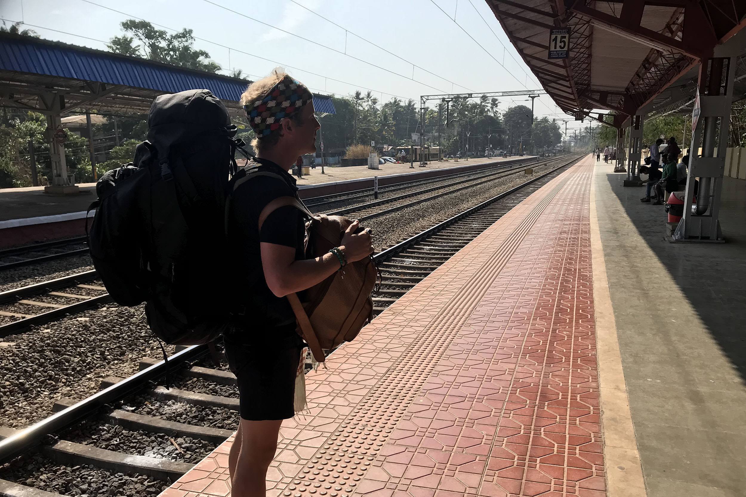 Ben with a Kathmandu backpack on the platform of a train station in Kerala India