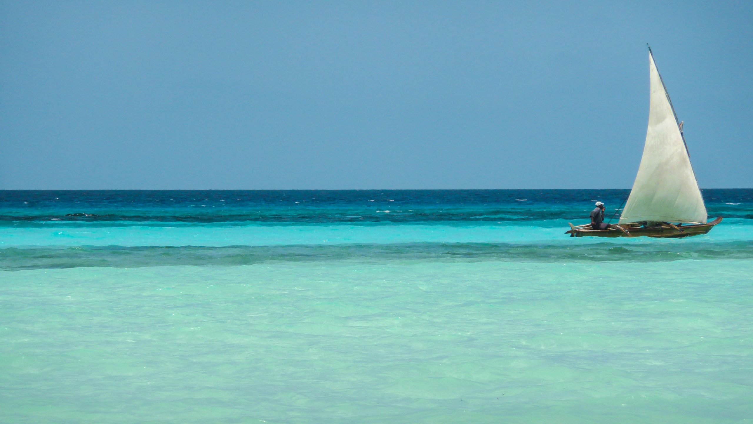 Dugout canoe with sail on turquoise water near Zanzibar beach Tanzania