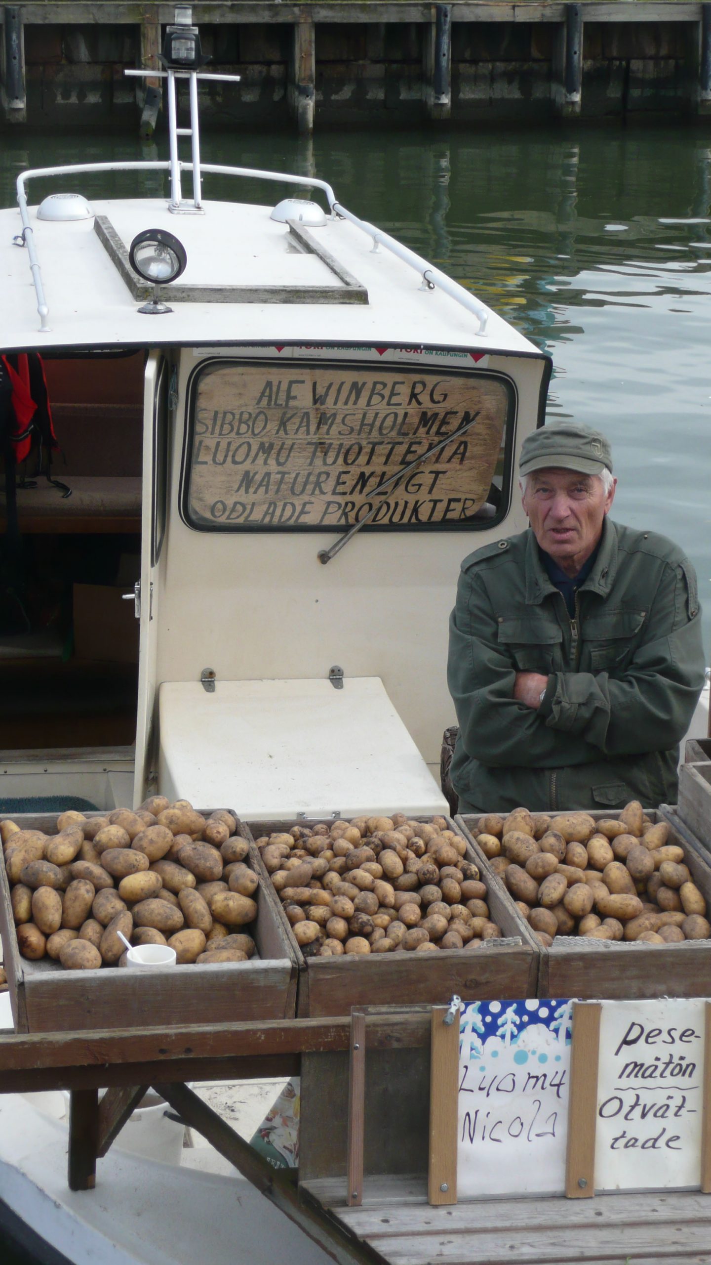 Elderly Finnish man sitting by boat in Market Square Helsinki Finland selling potatoes