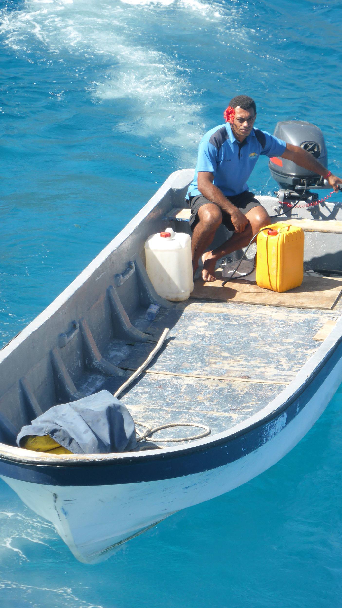 Fijian man with flower behind ear operating longboat in Fiji