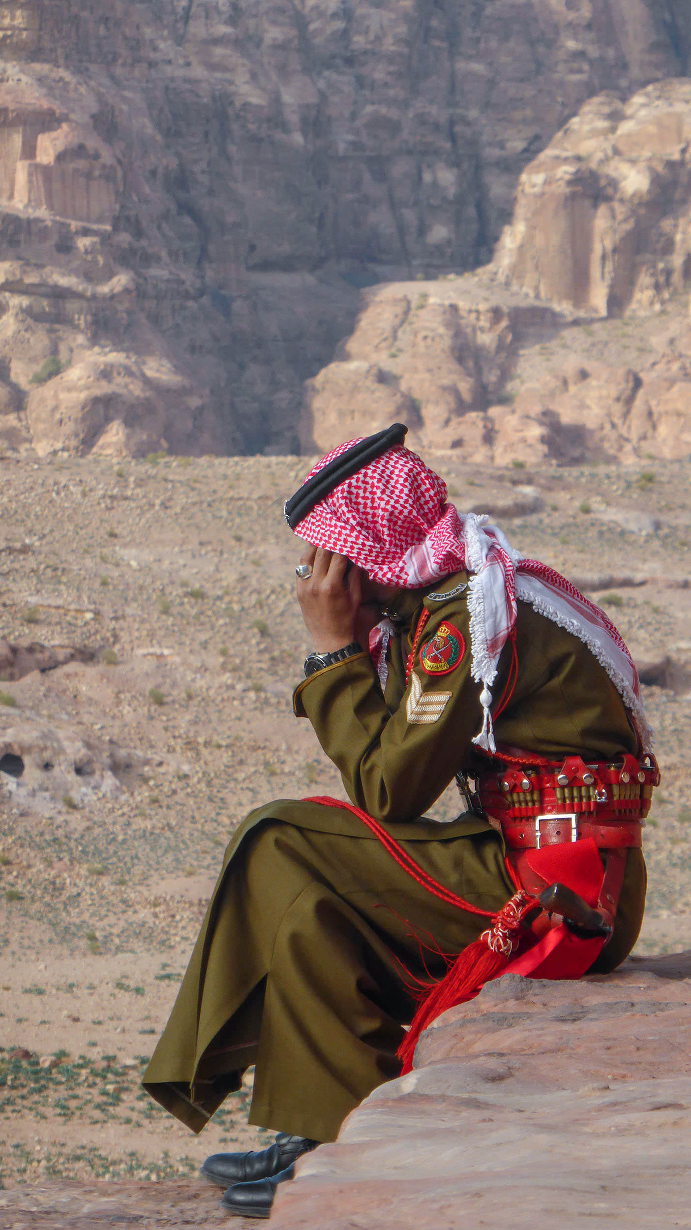 Jordanian man on phone sitting on cliff edge in Petra Jordan