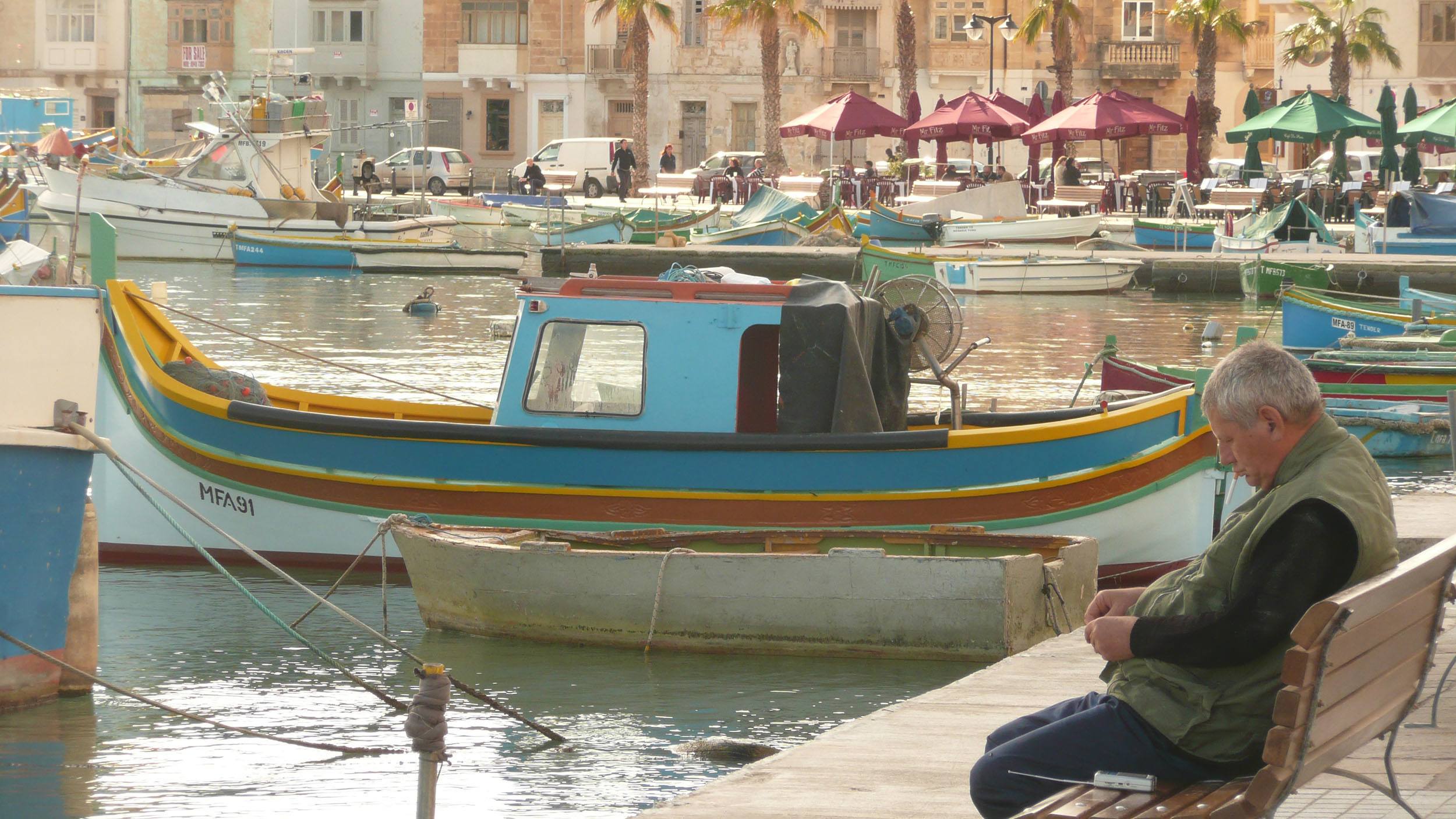 Man sitting on bench near water in Marsaxlokk Malta