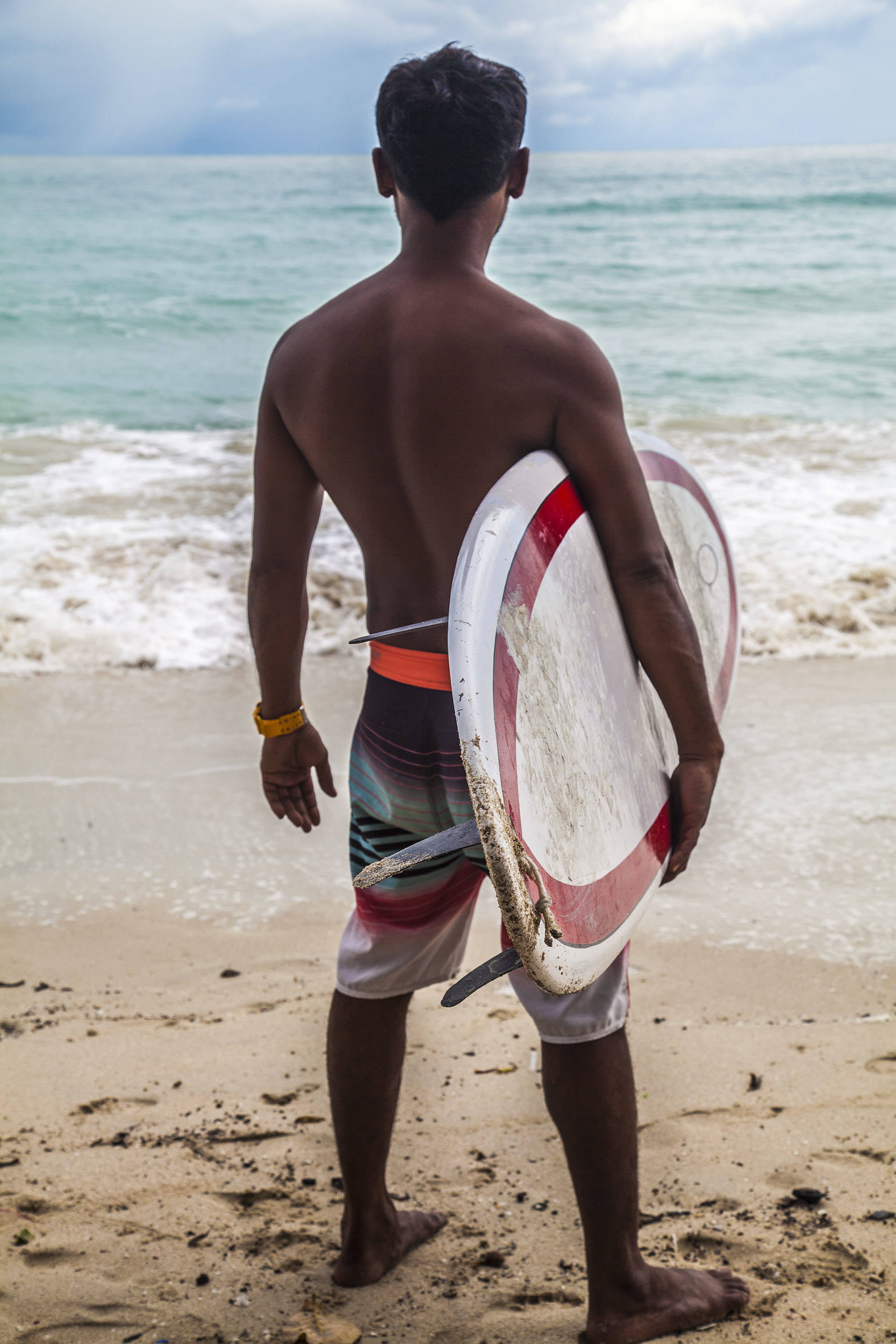 Thai man with surfboard under his farm facing water on Chaweng Beach Koh Samui Thailand