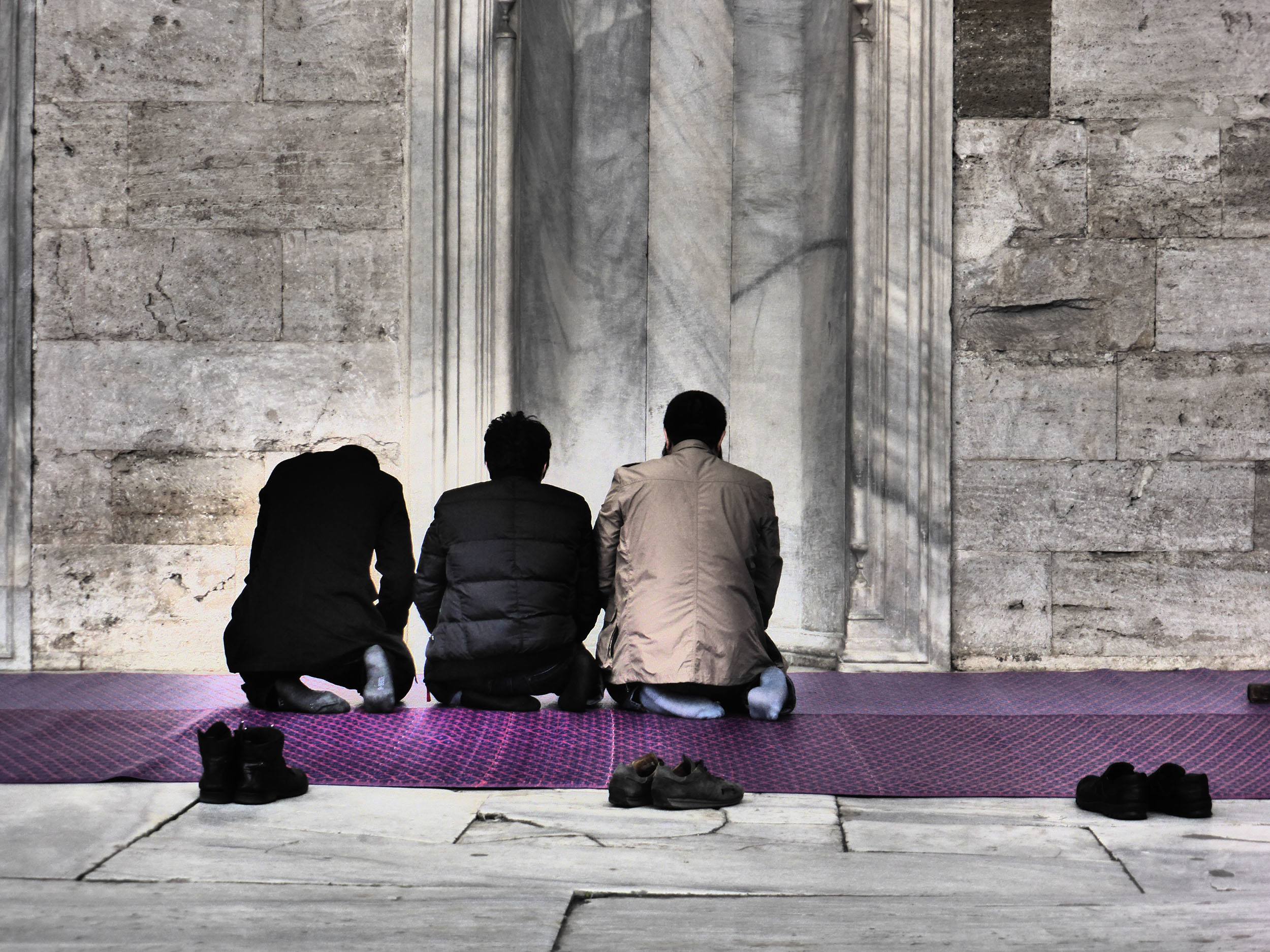 Turkish men kneeling on purple mat outside mosque in Istanbul Turkey