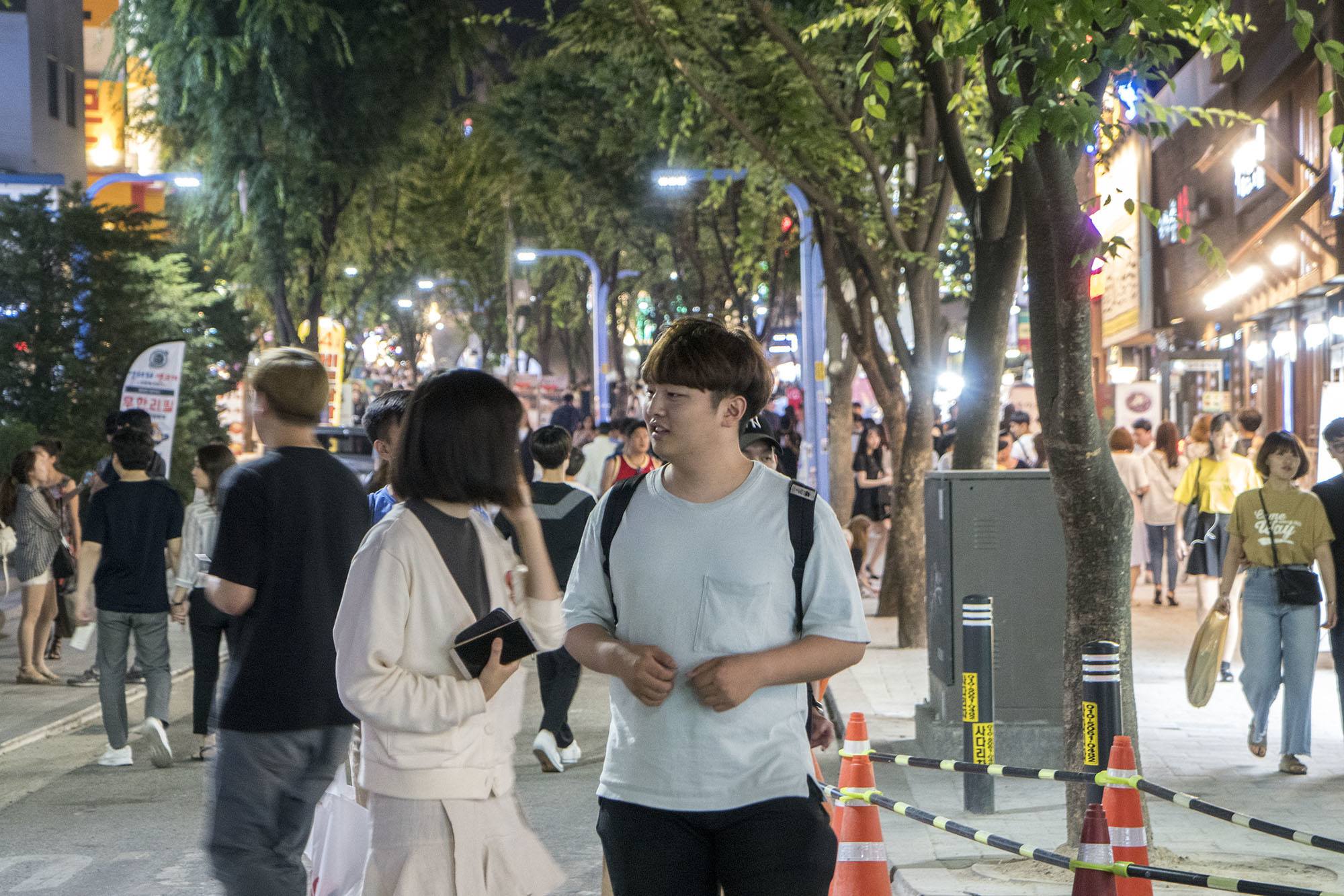 Korean man and woman walking through shopping street of Hongdae at night Seoul South Korea