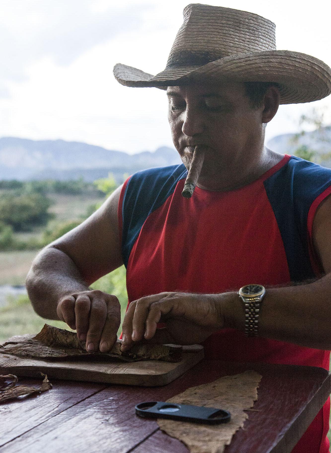 A Cuban man rolling a cigar while smoking one in the mountains near Vinales Cuba