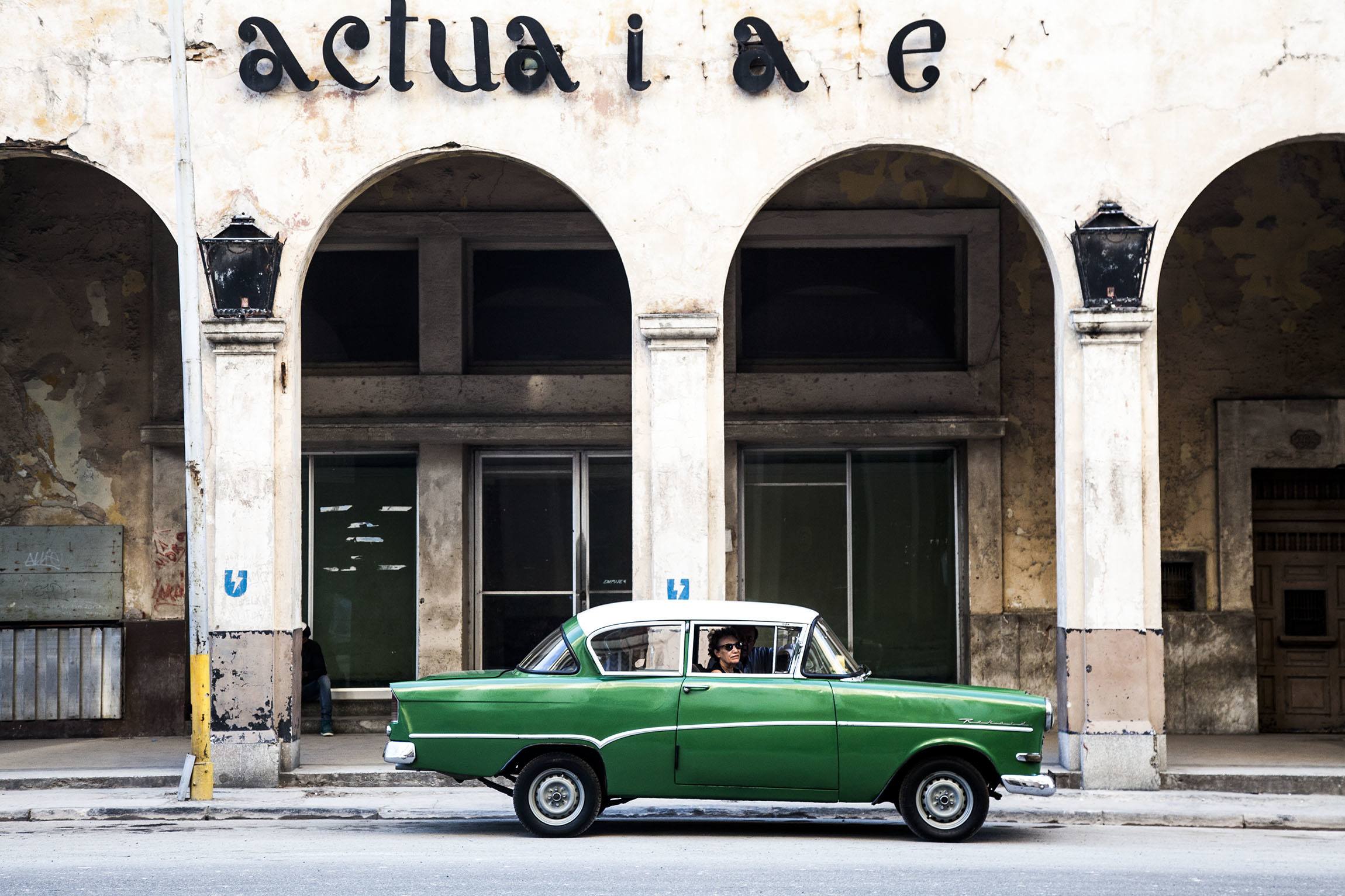 A classic green car parked in front of an archway of a building in Havana Cuba