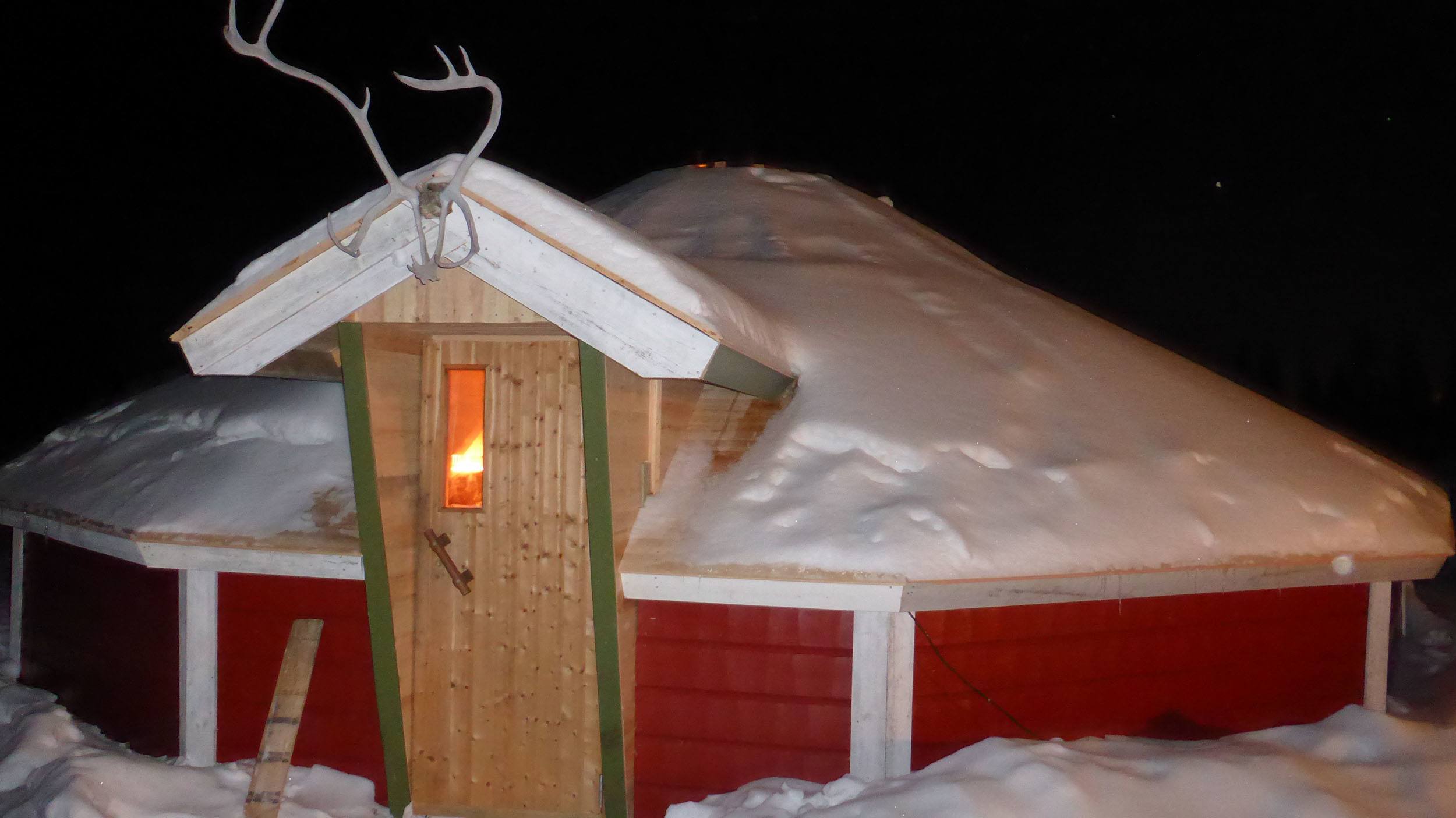 A large communal cabin at Camp Alta Sweden photographed during the night containing a fire and chimney