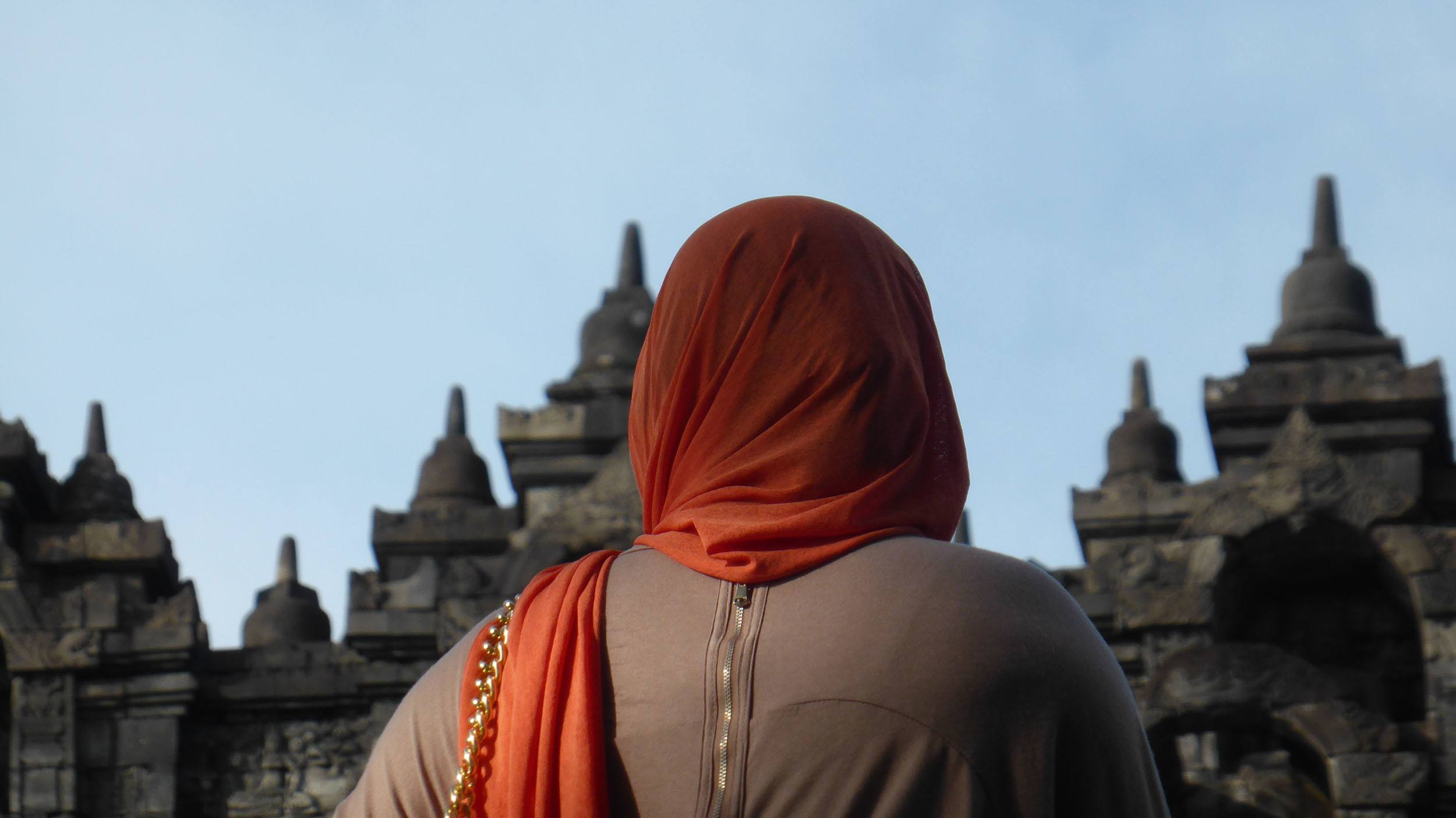 A woman wearing an orange shawl over her head at Borobodur Indonesia