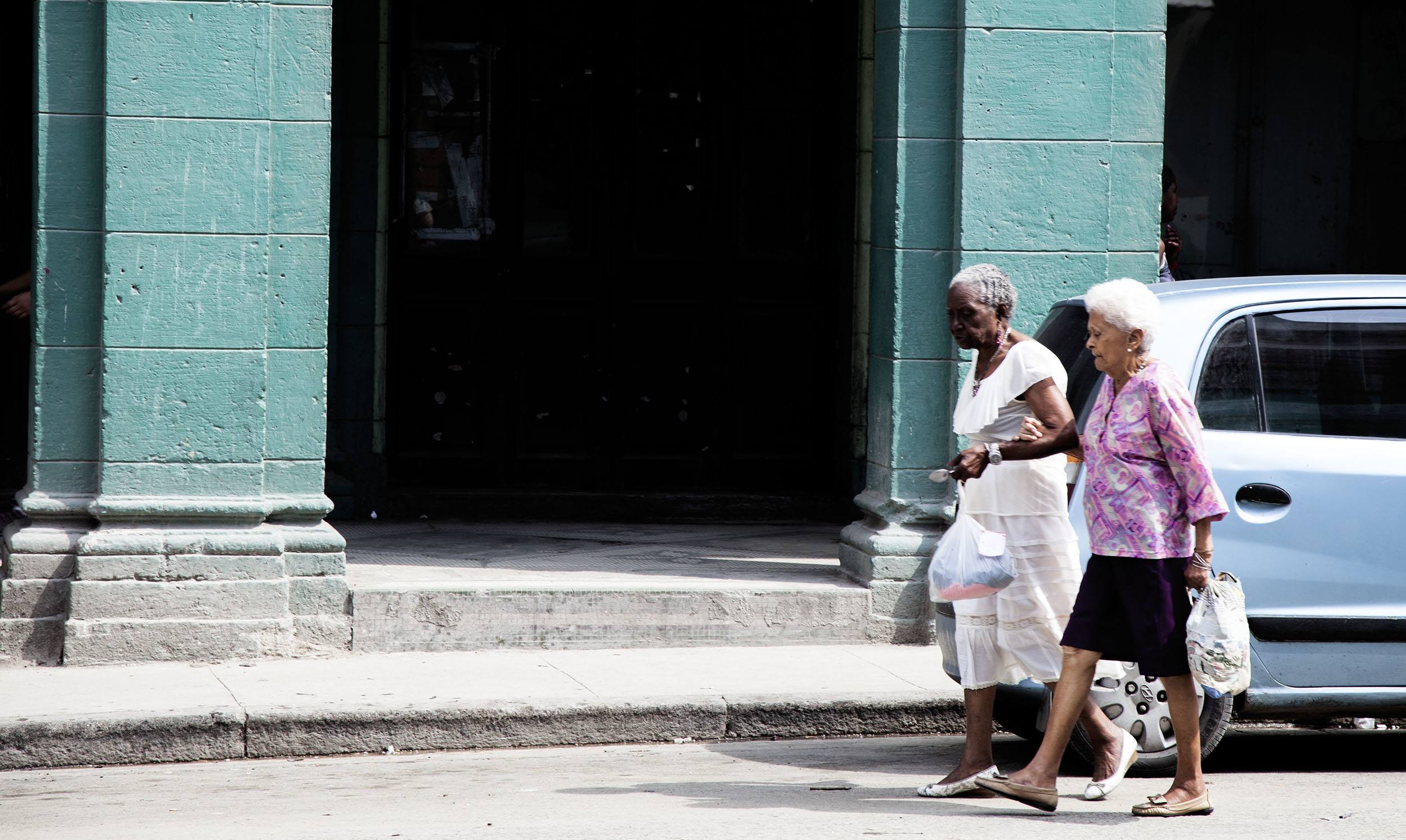 Elderly Cuban women helping one another walk along a street in Havana Cuba