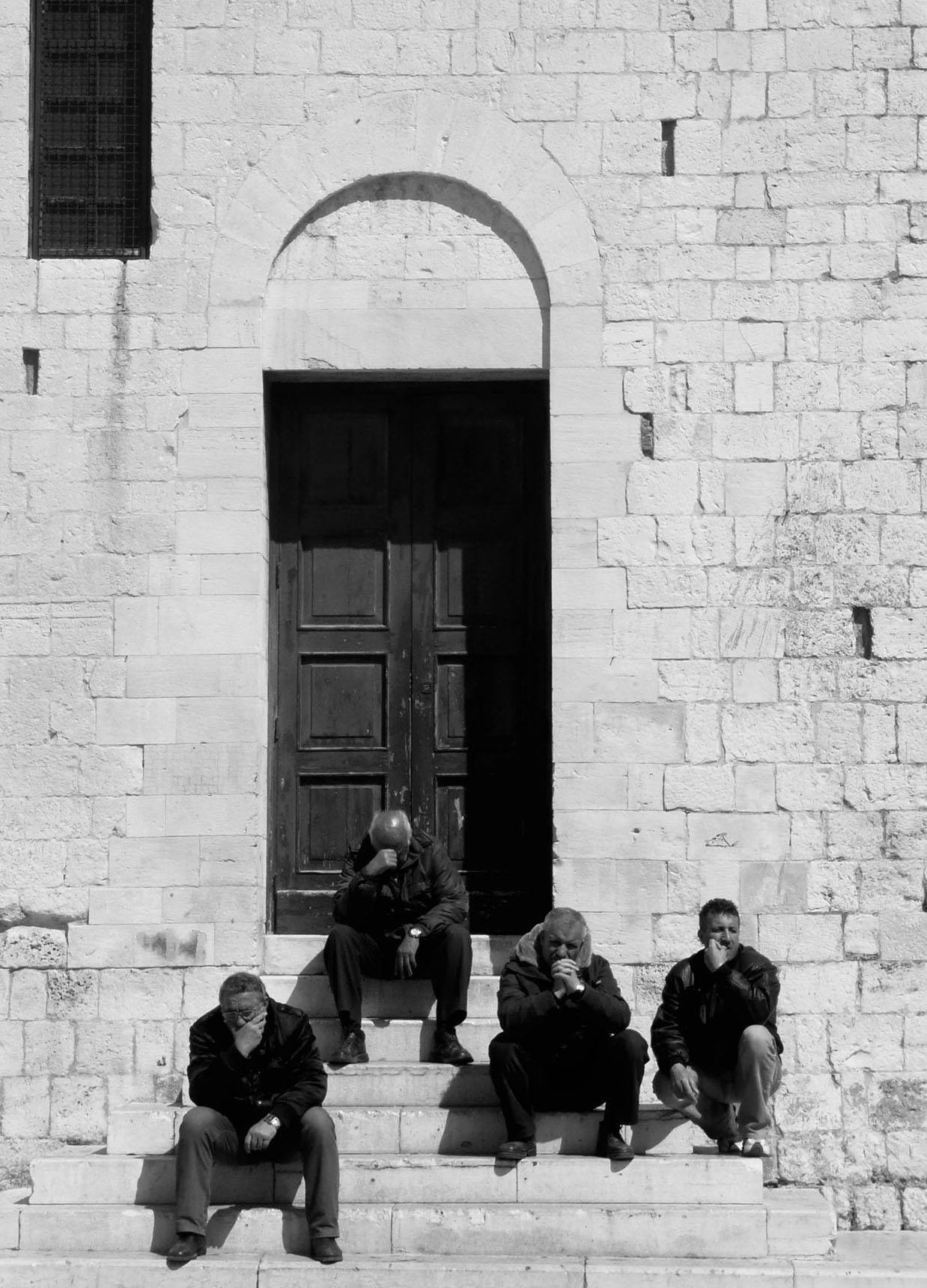 Italian men sitting on the steps of a building in a piazza in Bari Italy