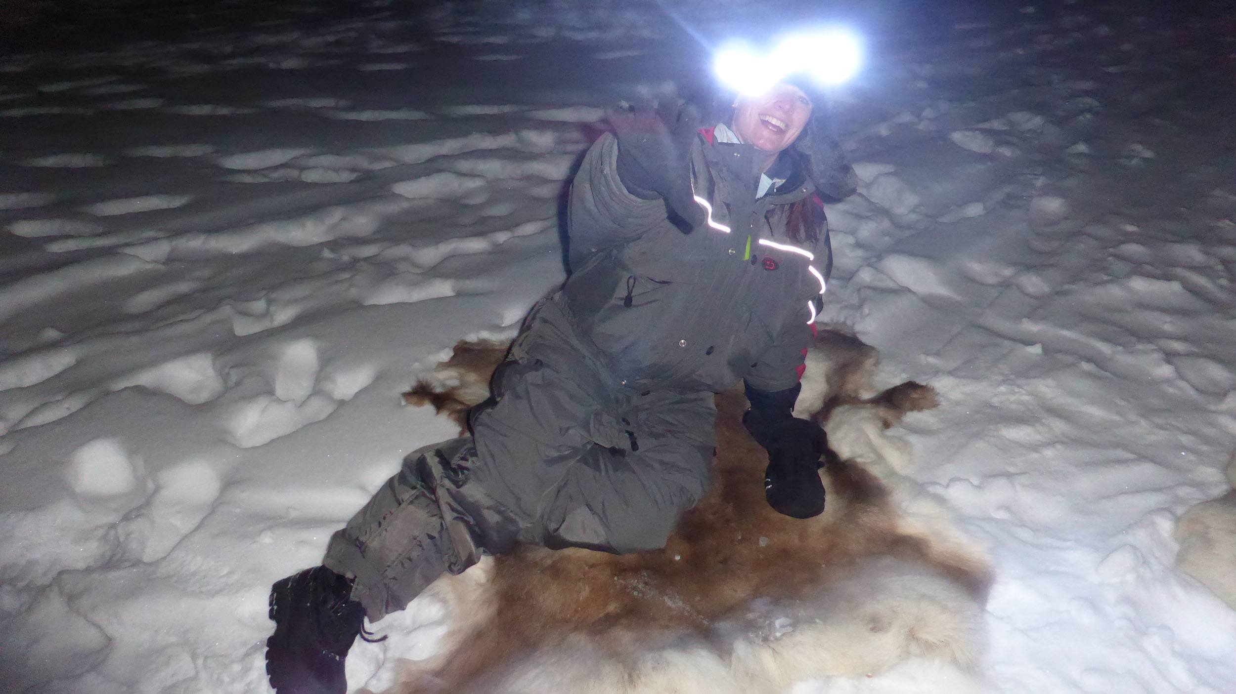 Kylie lying on a reindeer skin while ice fishing at Camp Alta in Sweden