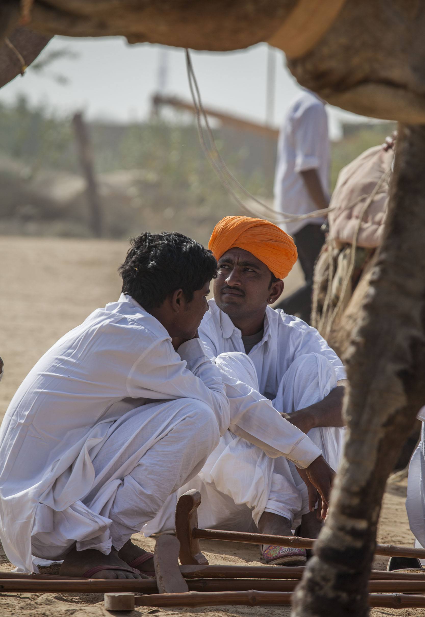 Man in orange turban sitting on the sand at the Jaisalmer Desert Festival in India