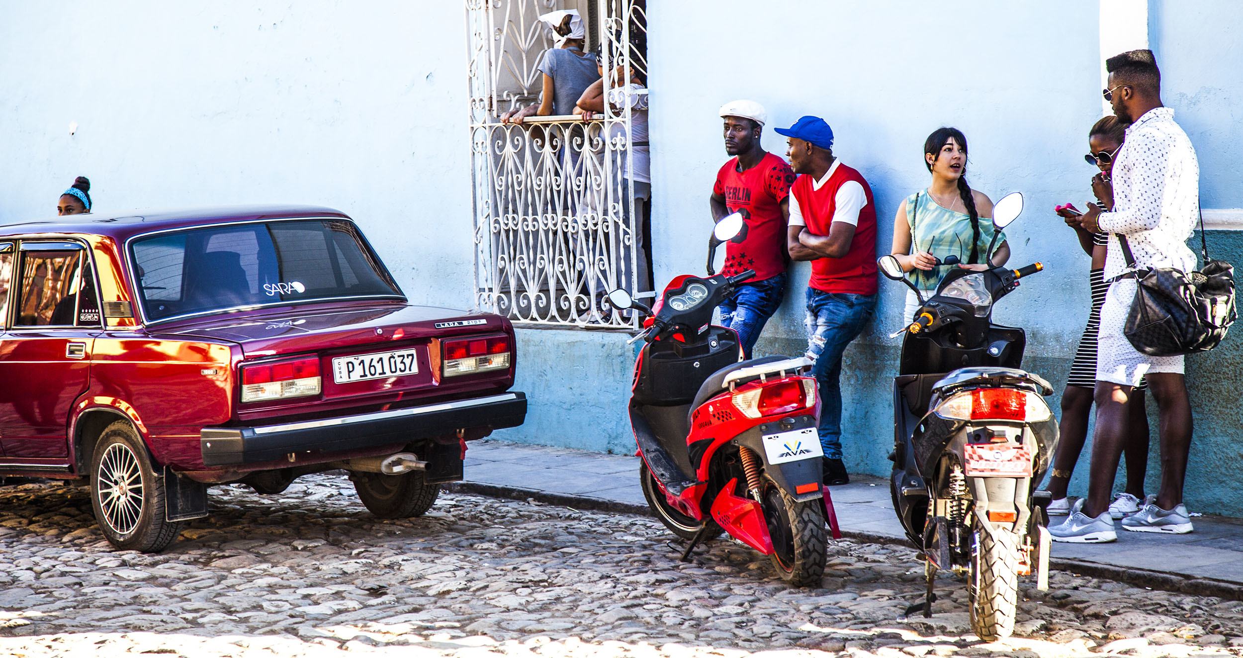 People congregating by a blue wall near a church in Trinidad Cuba