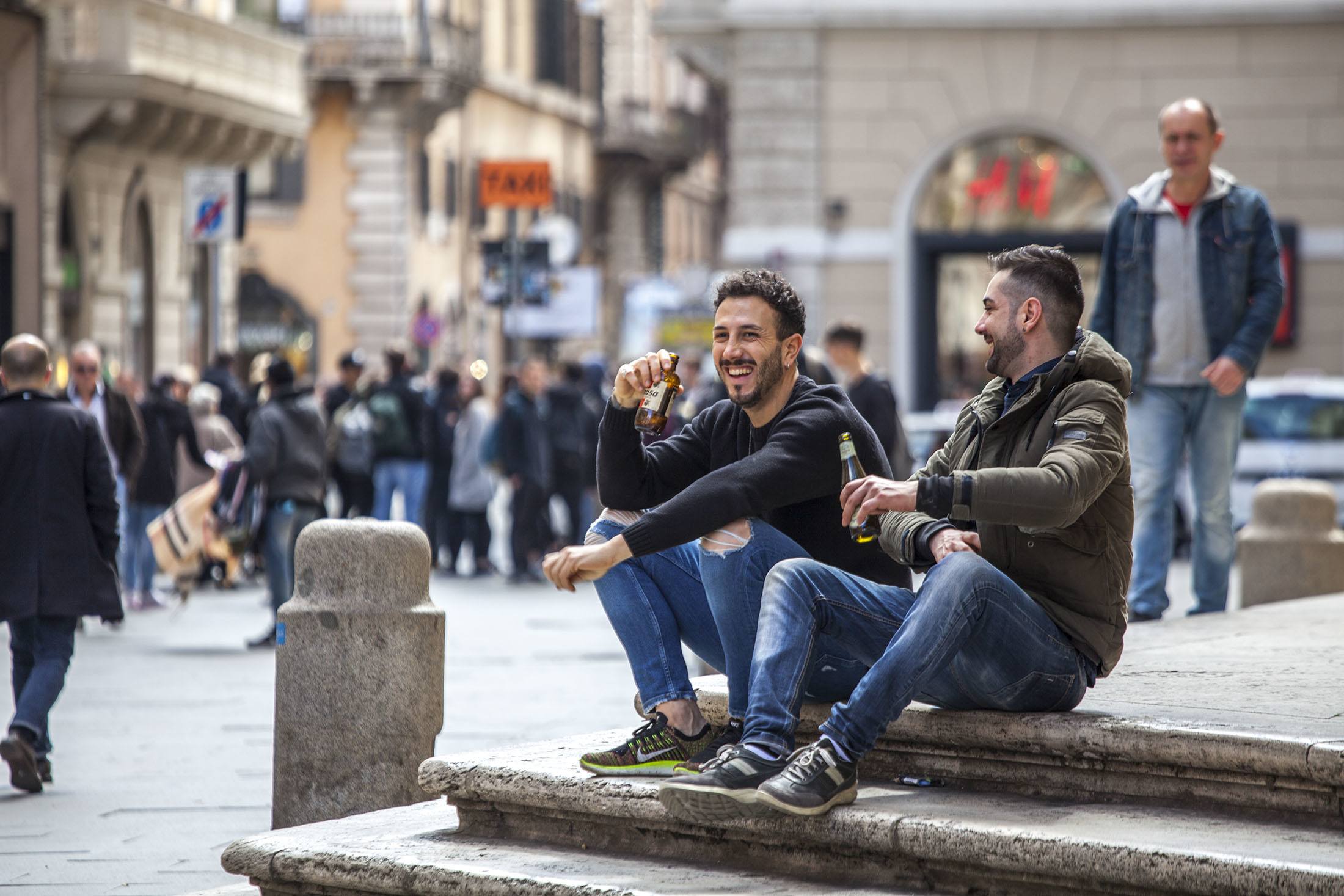 Two Italian men drinking on the steps of an ancient building alone Via del Corso in Rome Italy