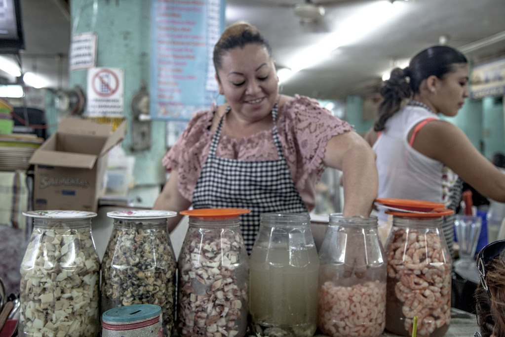 Woman with hand in jar of prawns at a market in Merida Mexico
