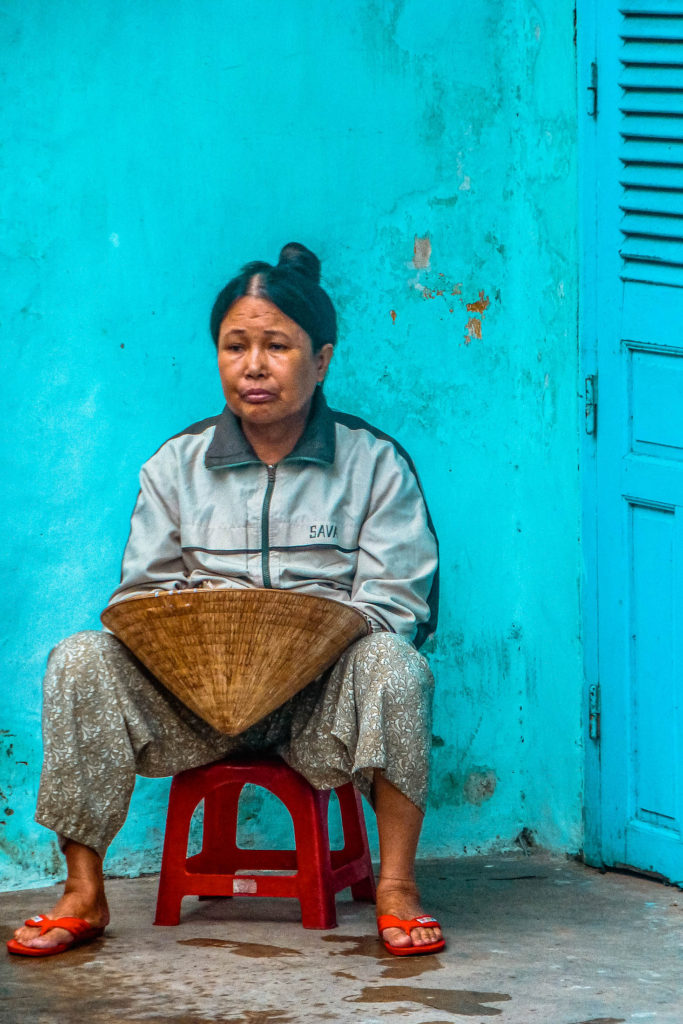 A woman holding a hat against a blue wall in Hoi An, Vietnam