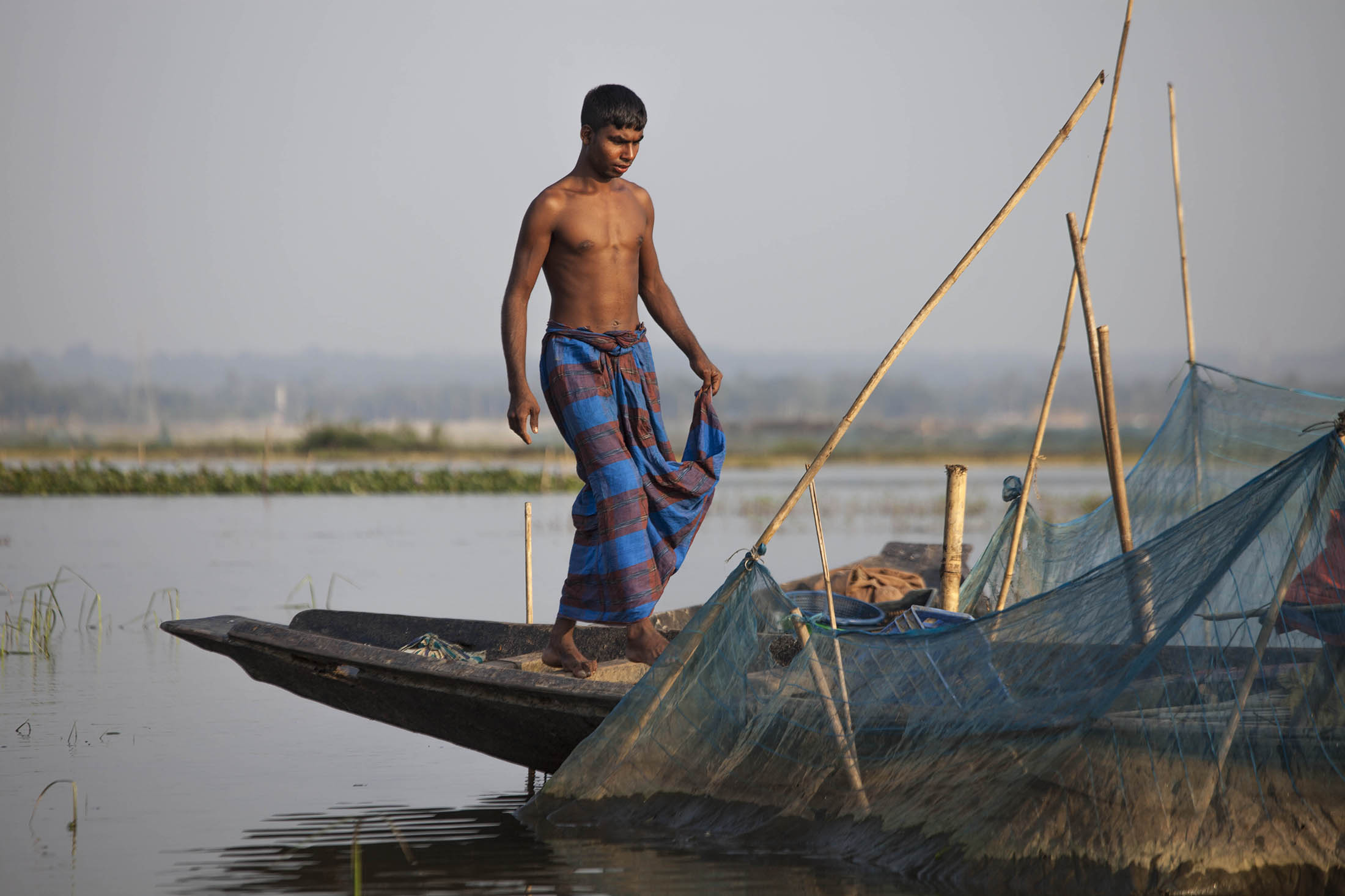 Shirtless young man on fishing boat on waterways near Sreemangal, Bangladesh