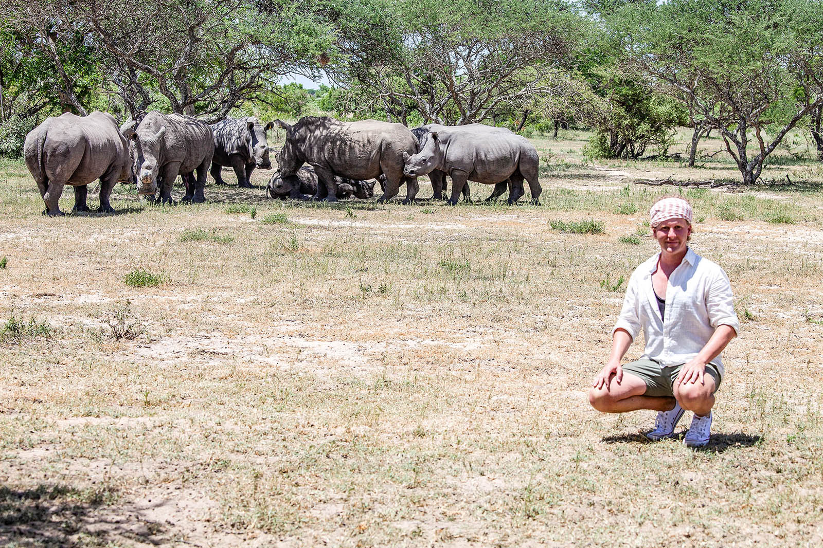 Ben squatting before white rhinos in Matobo National Park, Zimbabwe