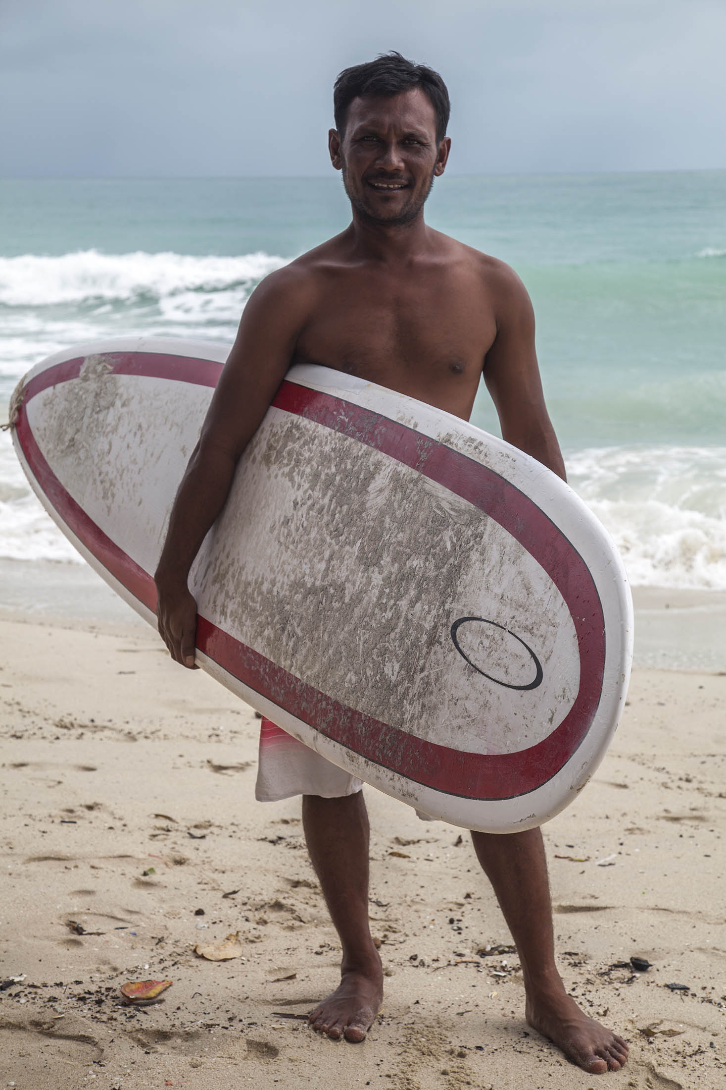 Thai man with surfboard under his arm on Chaweng Beach on Koh Samui Thailand